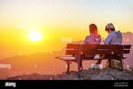 two-people-couple-sitting-together-on-a-bench-at-the-top-of-a-mountain-looking-at-the-sunset-d...jpg